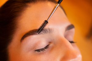 Close-up of a woman having her eyebrows groomed with a spoolie brush during a makeup session.