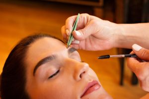 Professional makeup artist tweezing and grooming a client’s eyebrows during an eyebrow shaping session.